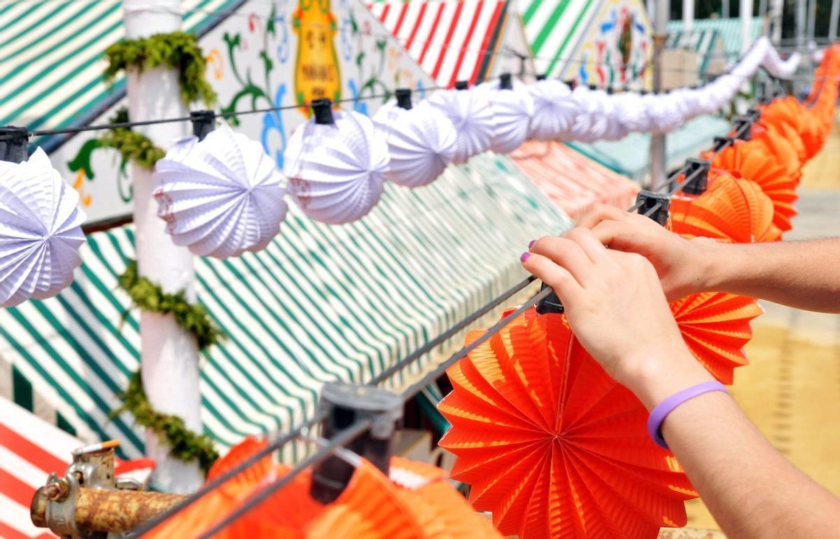 Una persona cuelga farolillos en una feria de Andalucía.
