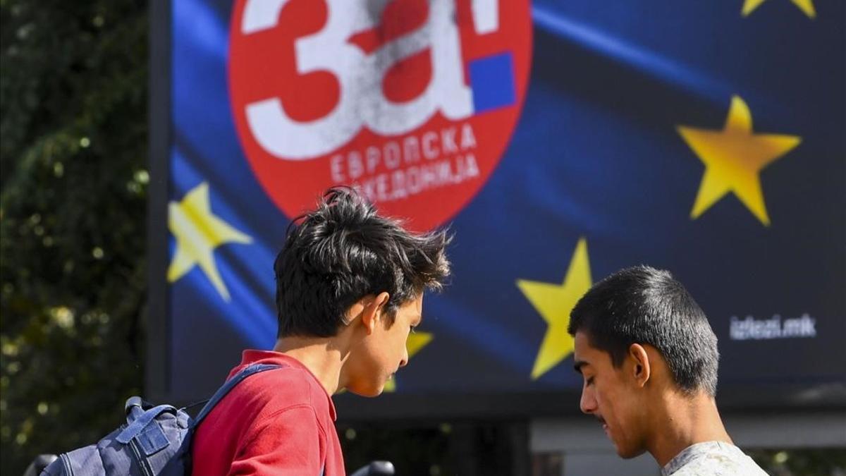 Dos chicos macedonios conversan junto a unos carteles con la bandera de la UE de la campaña a favor del 'sí' al referéndum.