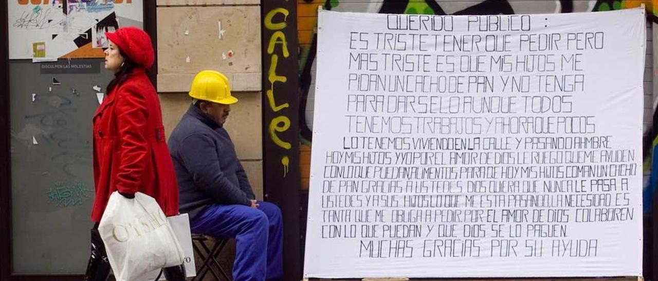 Una persona con un mensaje de petición de ayuda para vivir, en una calle comercial del centro de Gijón.