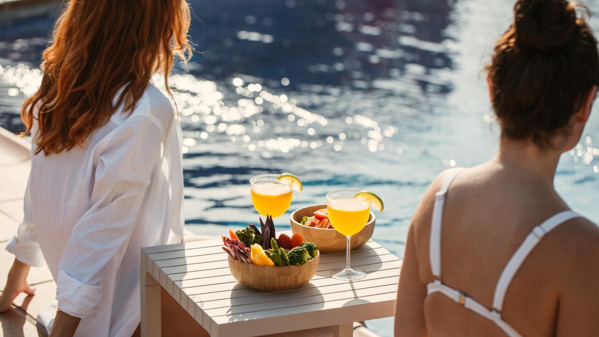 Dos mujeres disfrutan de un cóctel y un aperitivo en la piscina de Hyde Ibiza.