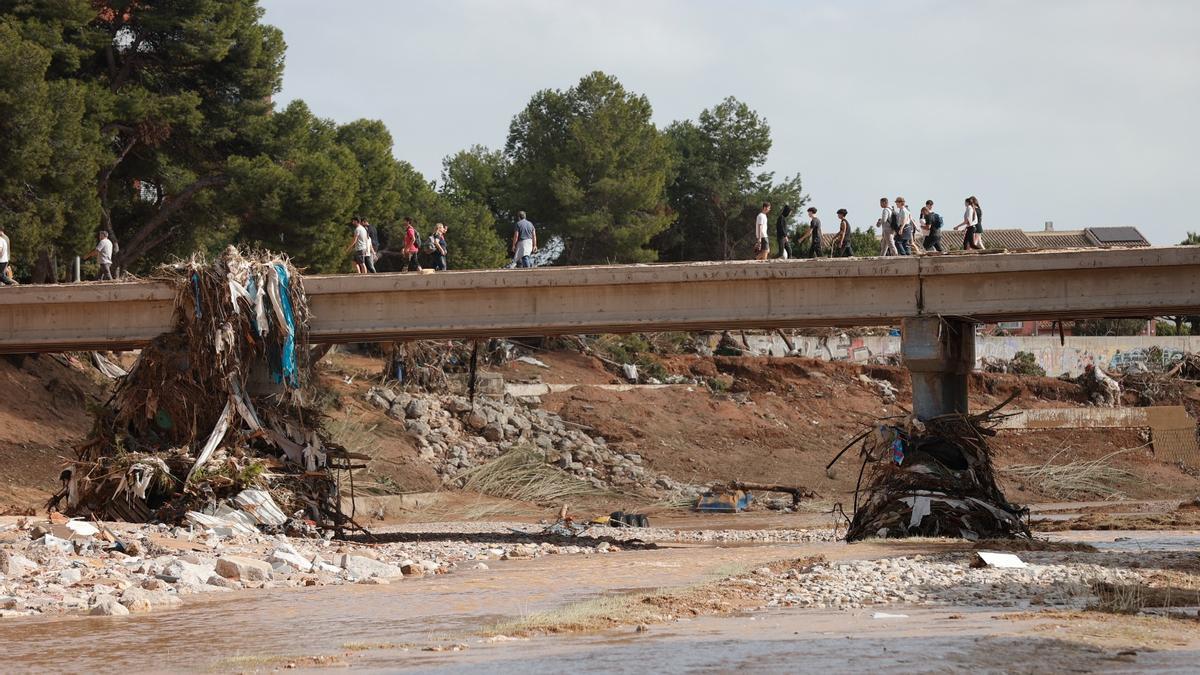 Peatones atraviesan uno de los puentes de Paiporta sobre el barranco del Poyo que sigue en pie.