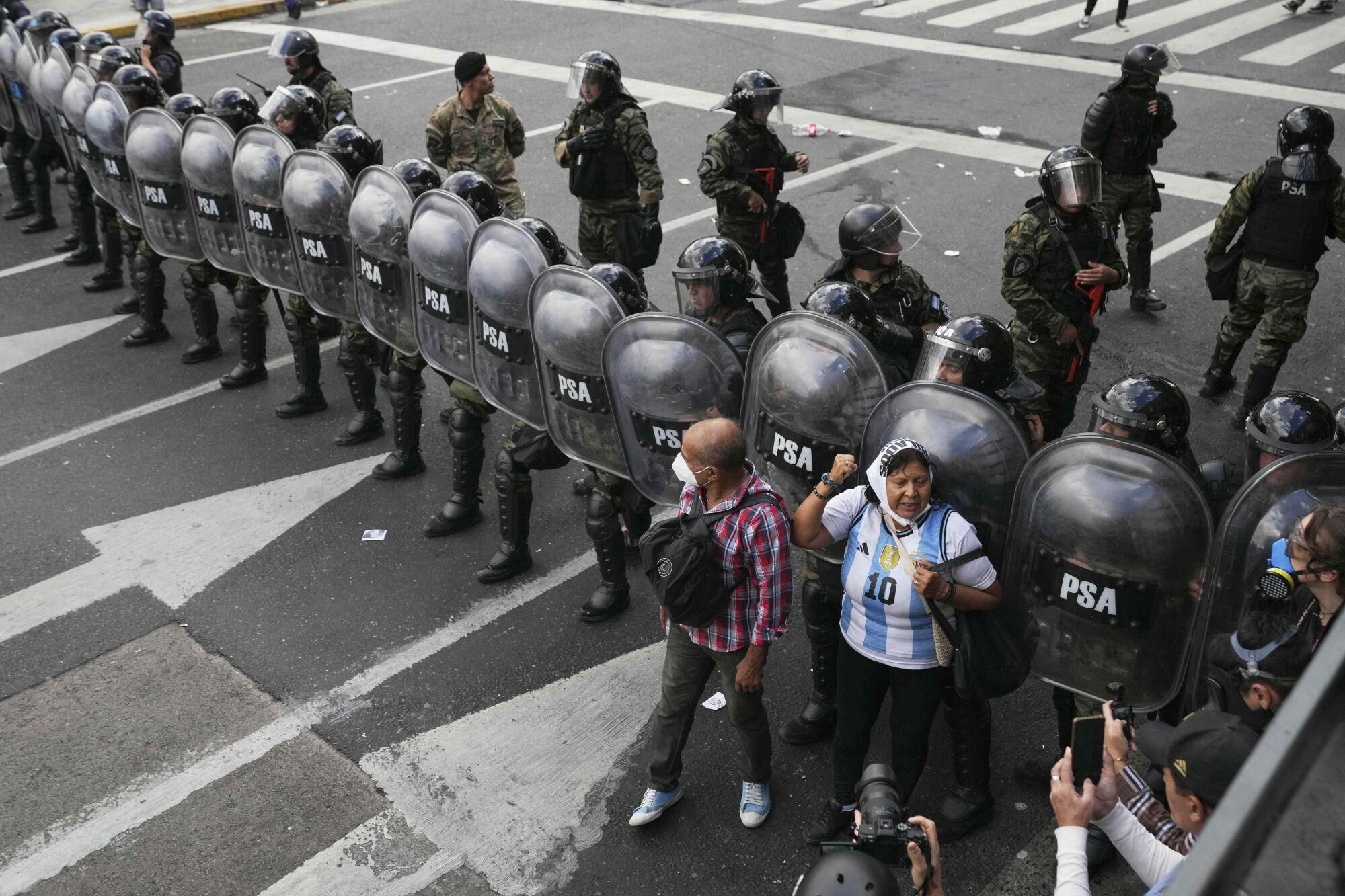 People stand in front of riot police during a protest by soccer fans and retirees demanding higher pensions and opposing austerity measures implemented by Javier Milei's government in Buenos Aires, Argentina, Wednesday, March 12, 2025. (AP Photo/Natacha Pisarenko). EDITORIAL USE ONLY/ONLY ITALY AND SPAIN