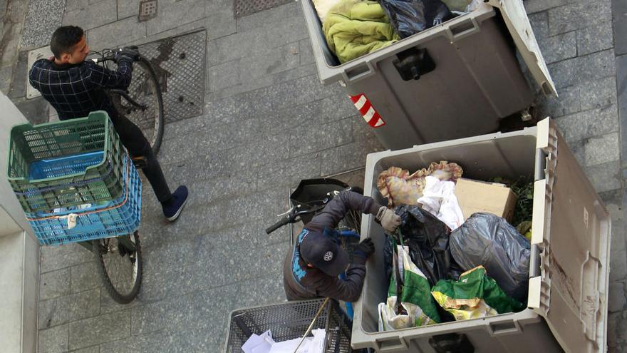 Jóvenes rebuscan en la basura, en contenedores del centro de Valencia.