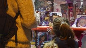 Una niña observa el escaparate de una juguetería junto a su padre.