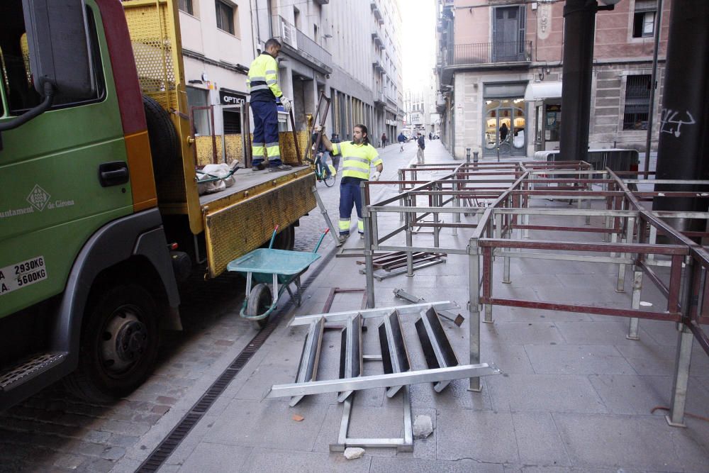 Carrers amb restes de mobiliari urbà cremat, contenidors per terra i treballadors de la brigada treballant