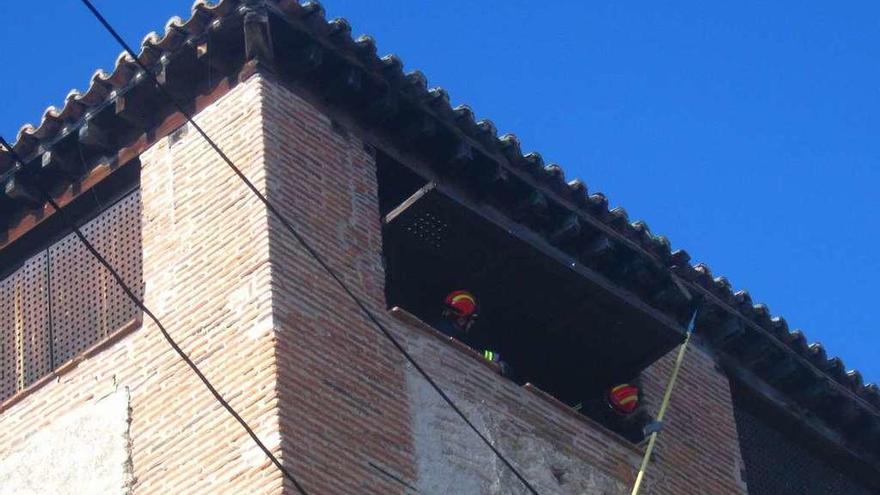 Dos bomberos retiran las tejas de la cubierta del torreón para evitar que caigan a la calle Arbas.