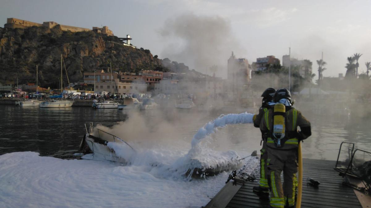 Dos bomberos apagando una embarcación en llamas en el puerto pesquero de Águilas.
