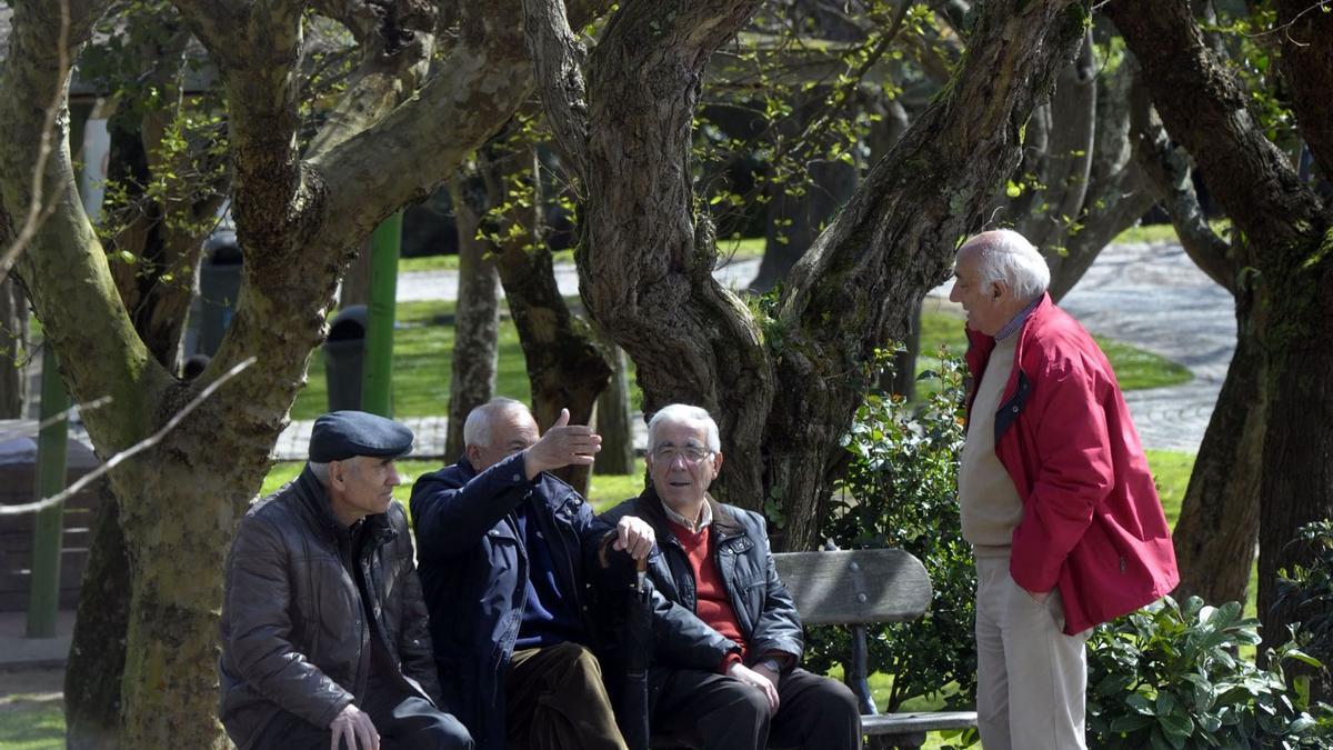 Un grupo de jubilados conversa animadamente sentados en el banco de un parque público.