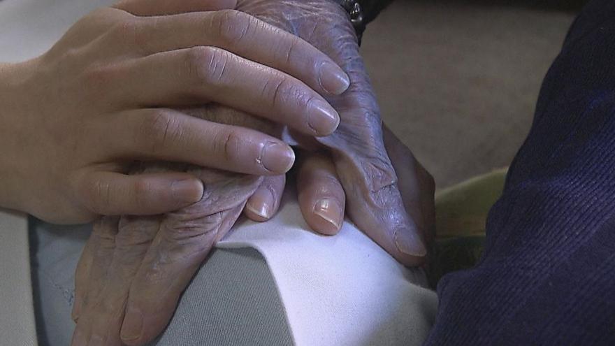 Una persona le da la mano a otra mayor en un centro hospitalario.