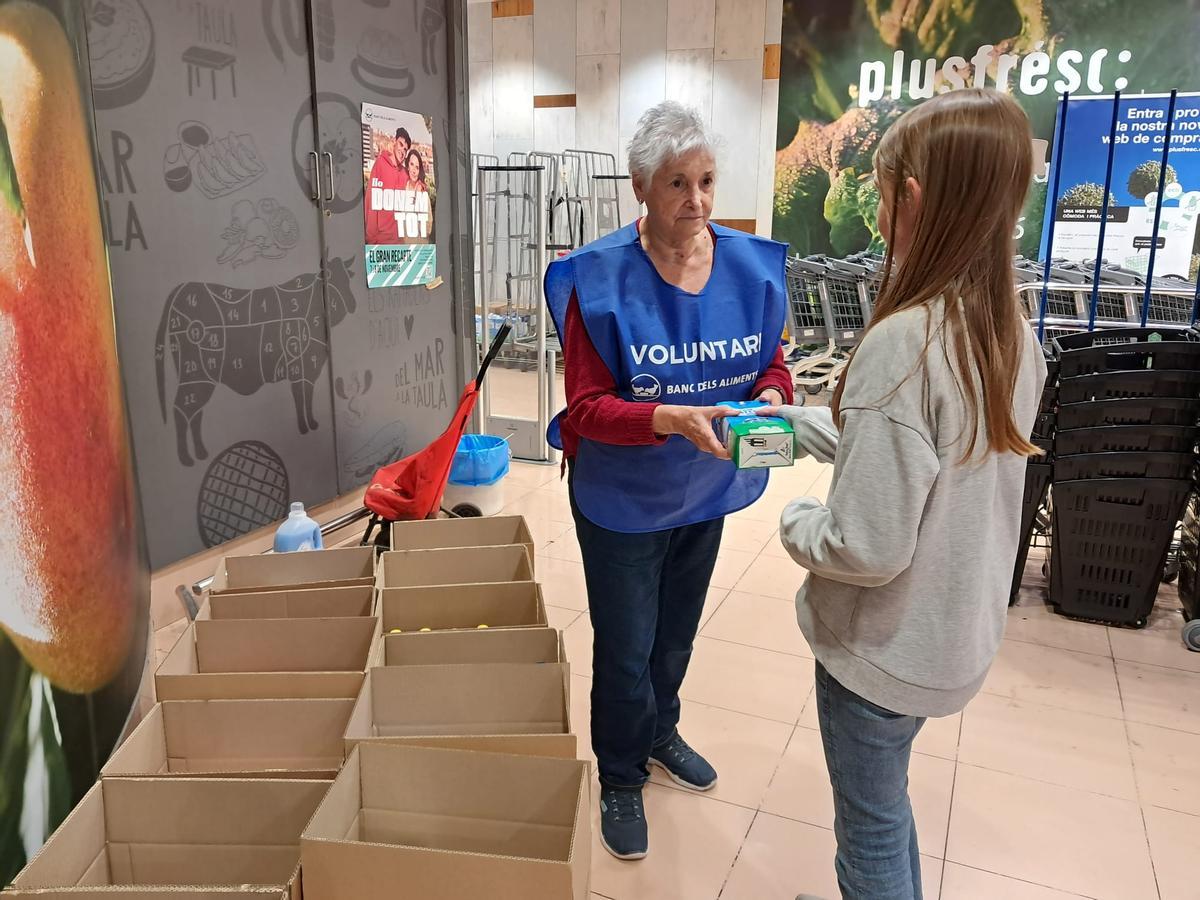 La voluntària Sara Barco rep un quilo de llet d'una nena que anava amb la seva mare i també ha volgut ajudar