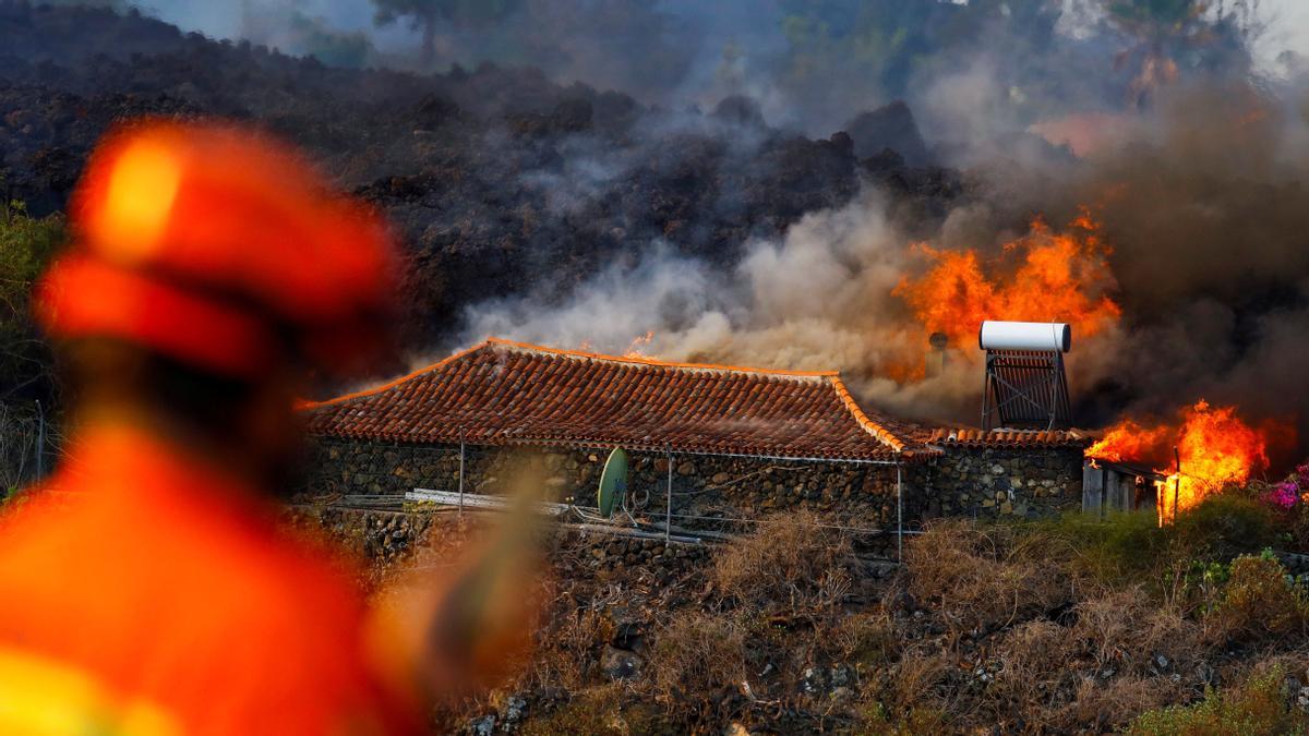 A member of Civil Protection watches as a house burns due to lava from the eruption of a volcano in Spain