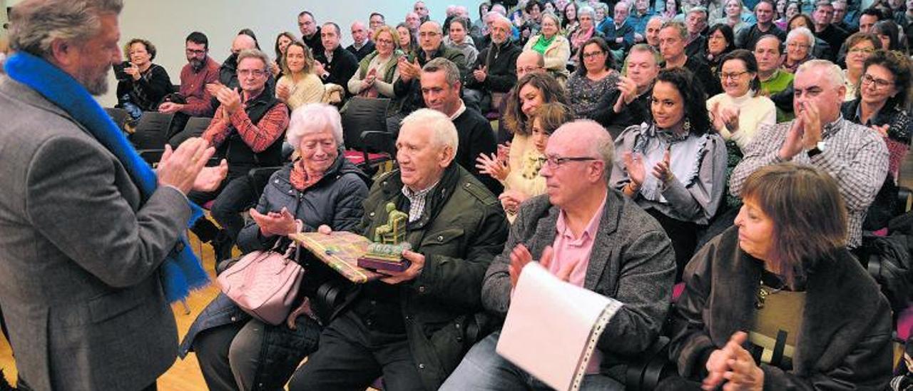 El escritor Alejandro Antúñez, con dos regalos en sus manos, recibe un aplauso durante el homenaje a su vida y obra, en Navia. | A. M. S.