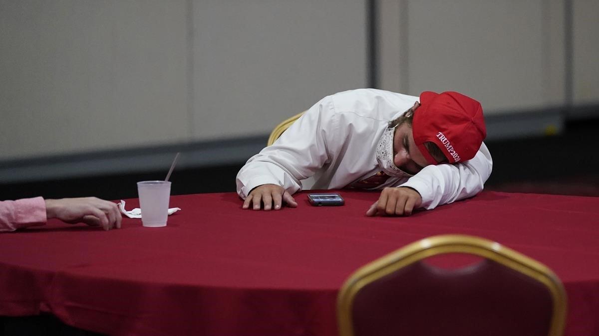Un partidario del presidente Donald Trump, descansa sobre una mesa mientras espera los resultados de las elecciones. 