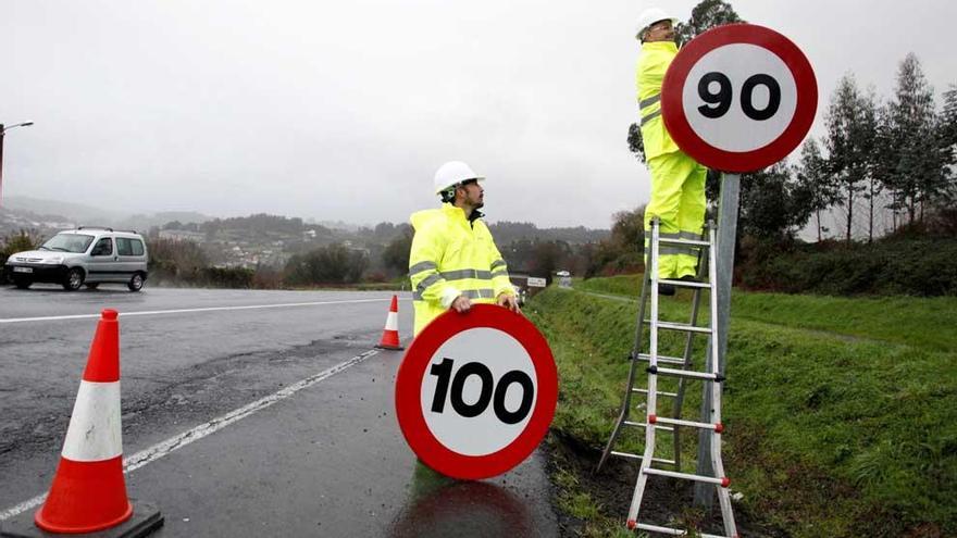 Dos operarios colocan una nueva señal del límite a 90 km/h.