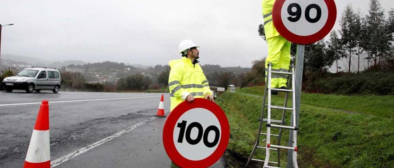 Dos operarios colocan una nueva señal del límite a 90 km/h.