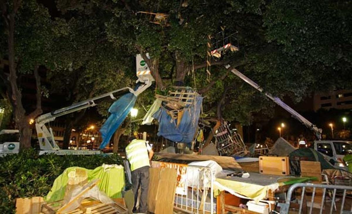 Els serveis de neteja de Barcelona s’ajuden de dues grues per retirar els trastos situats en un dels arbres de la plaça.