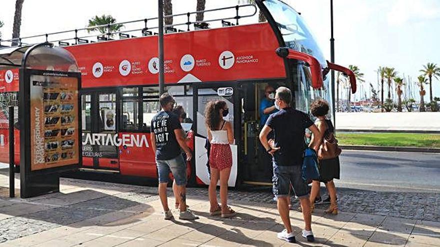 Pasajeros con mascarilla subiendo a un autobús turístico en Cartagena.