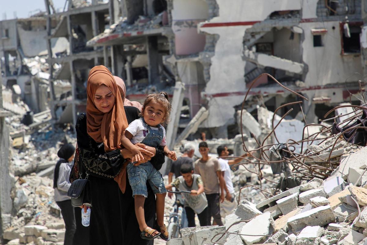 Una mujer camina, con su hija en brazos, por las ruinas de casas destruidas durante una ofensiva israelí en Jan Yunis, el el sur de Gaza.