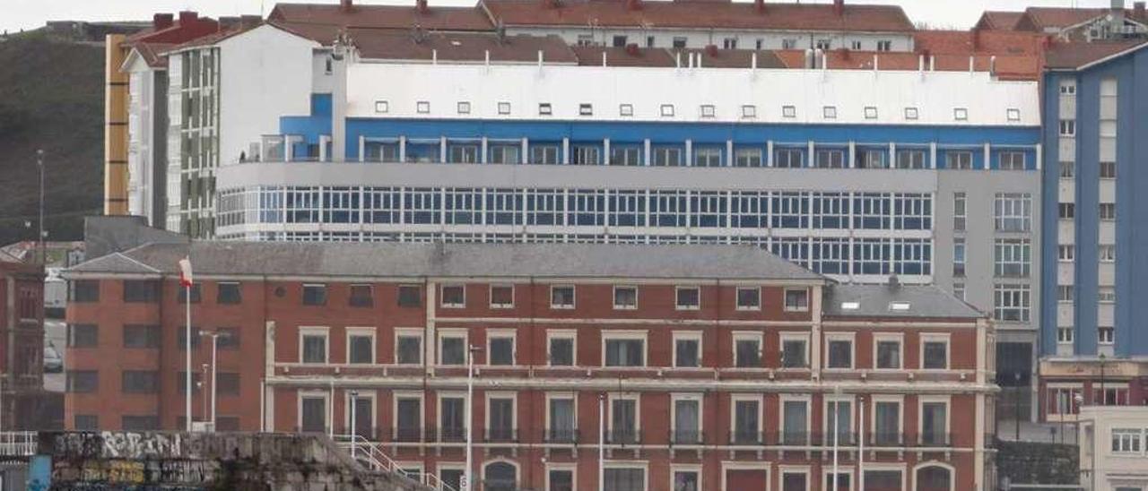 En primer término, el edificio de la antigua sede de la Autoridad Portuaria de Gijón, con viviendas del barrio de Cimadevilla tras él y el &quot;Elogio del Horizonte&quot; al fondo.