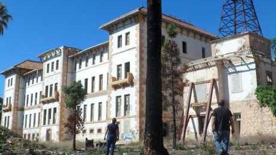 Una pareja pasea por el exterior del preventorio, con una palmera quemada en el incendio del pasado julio.