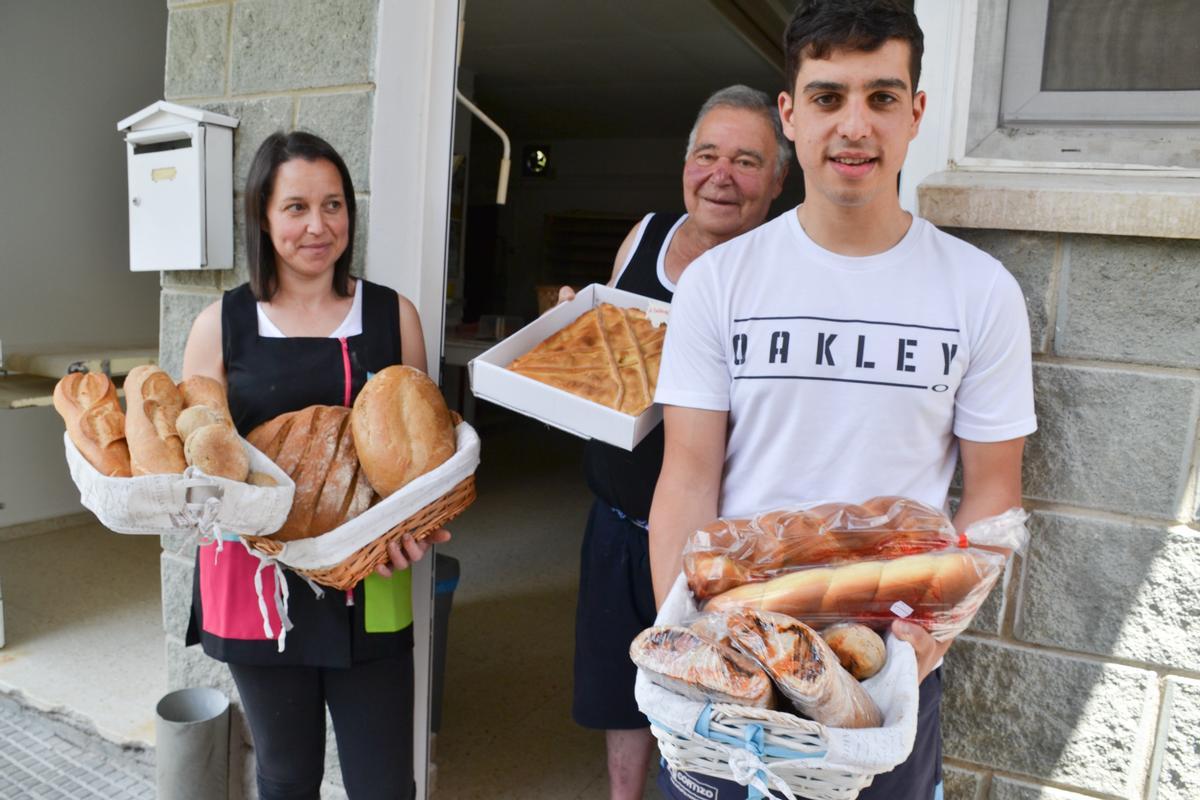 El joven profesional de Navelgas posa en exterior de la panadería familiar, con productos elaboradorados en la misma, en compañía de su madre y su abuelo.