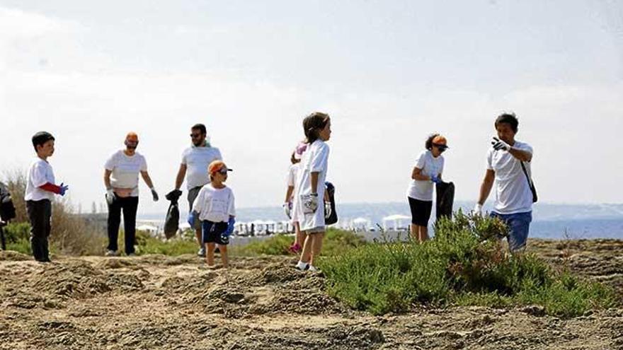 Varios niños y adultos en es Carnatge recogiendo los desperdicios que encuentran por el suelo.