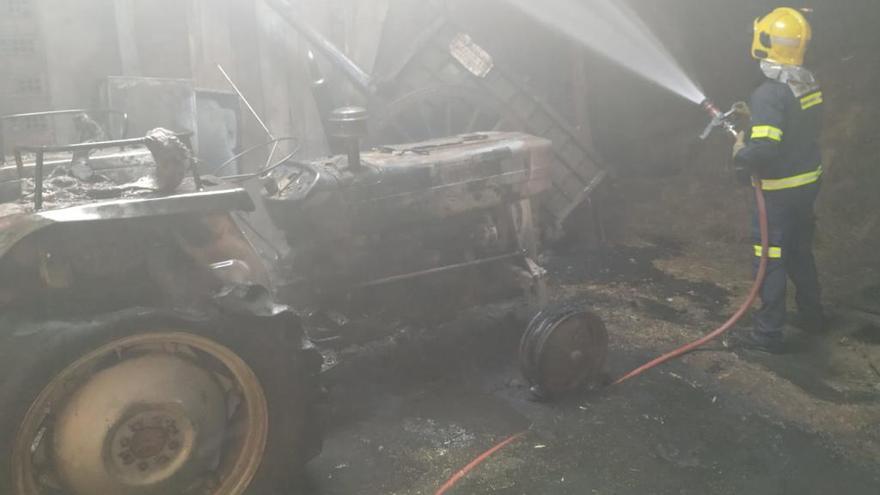 Un bombero termina de sofocar el incendio en la nave de Puercas de Aliste. A la izquierda, el tractor calcinado.