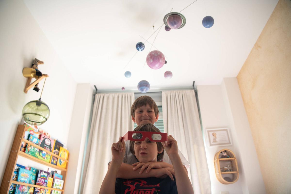 Mateo y Martín en su habitación, con un móvil de planetas que tienen en el techo y las gafas especiales para ver el eclipse del 12 de agosto. Sociedad. Barcelona, 7 de agosto de 2026. Foto: Belén González / EP