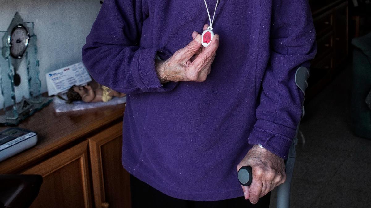 Una mujer muestra el botón rojo de teleasistencia que tiene, en su casa de Barcelona.