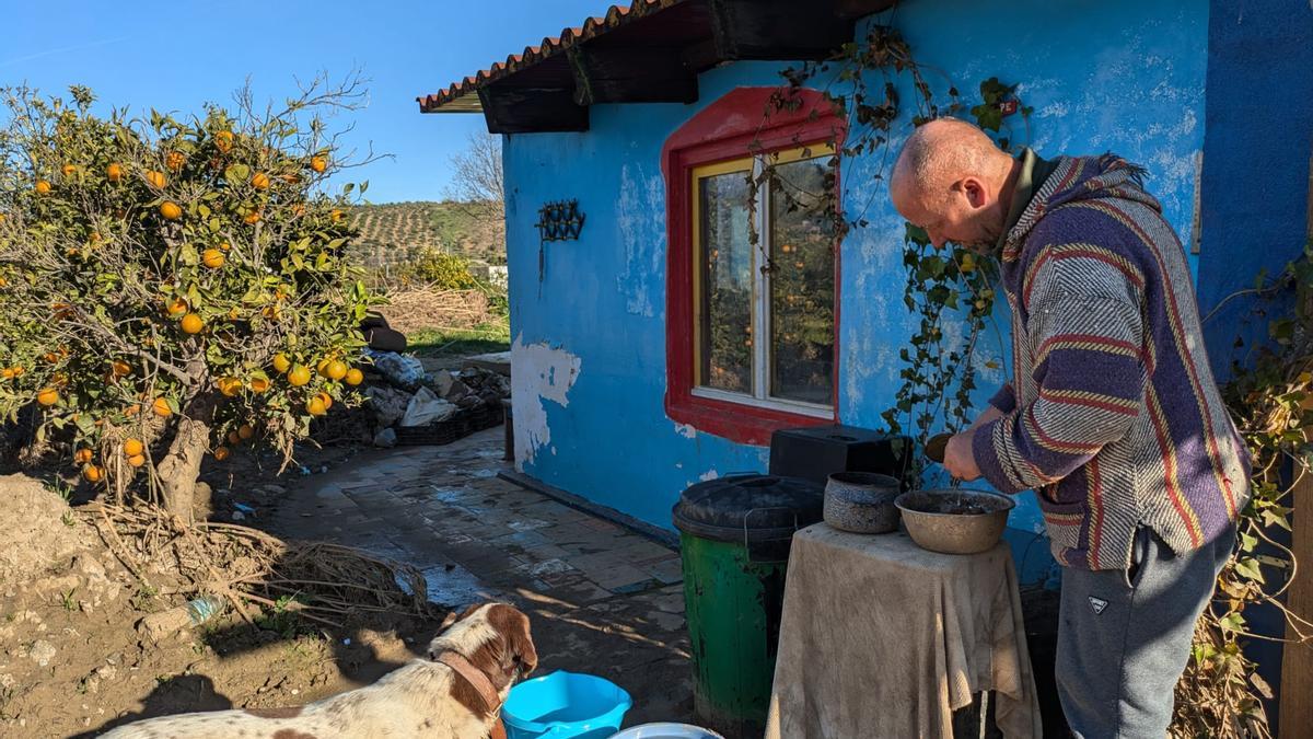 Patrick Van Riessen preparando la comida para sus perros, con la atenta mirada de Dina, en el patio de su hogar en Álora.