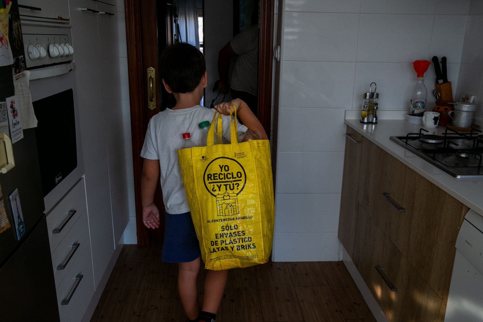 Un niño con una bolsa de plásticos y envases para reciclar.