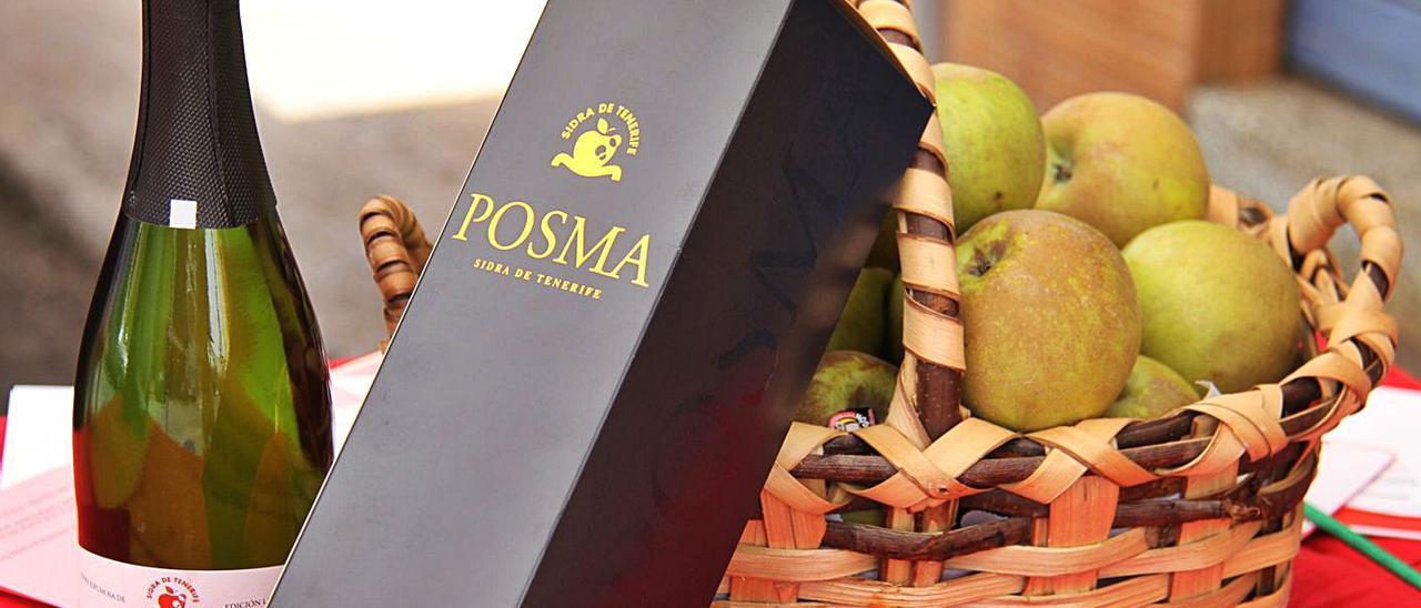 Una botella de sidra Posma, de El Sauzal, junto a un cesto lleno de manzanas reinetas.