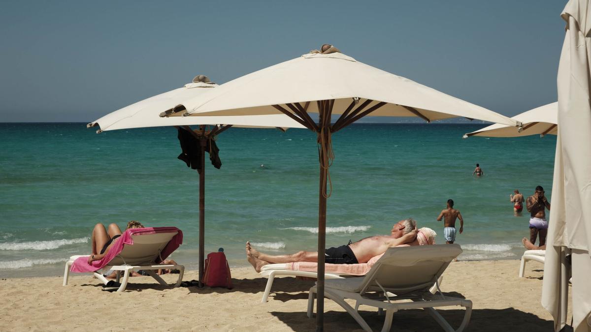 Turistas tomando el sol bajo unas sombrillas