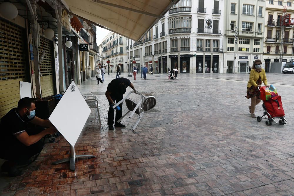 Imágenes de una lluviosa mañana de jueves en el centro de Málaga, donde al paisaje ya habitual de pocas personas y la mayoría de ellas con guantes y mascarillas se le han añadido los preparativos de bares, cafeterías y terrazas que se preparan para el inminente cambio de fase de la desescalada de la ciudad.