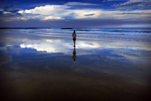 Storm clouds and dust can be seen in the sky above a woman as she walks at dusk along Mollymook Beach