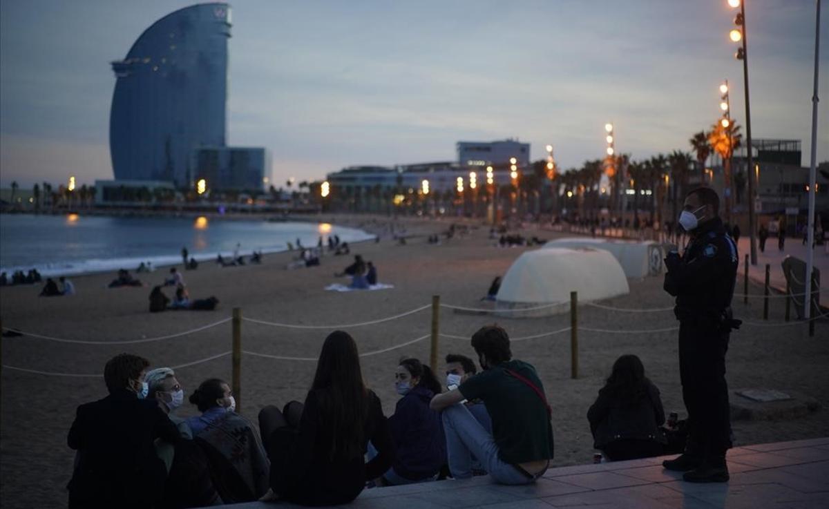 Un agente junto a un grupo de jóvenes, al atardecer, en la playa de la Barceloneta.