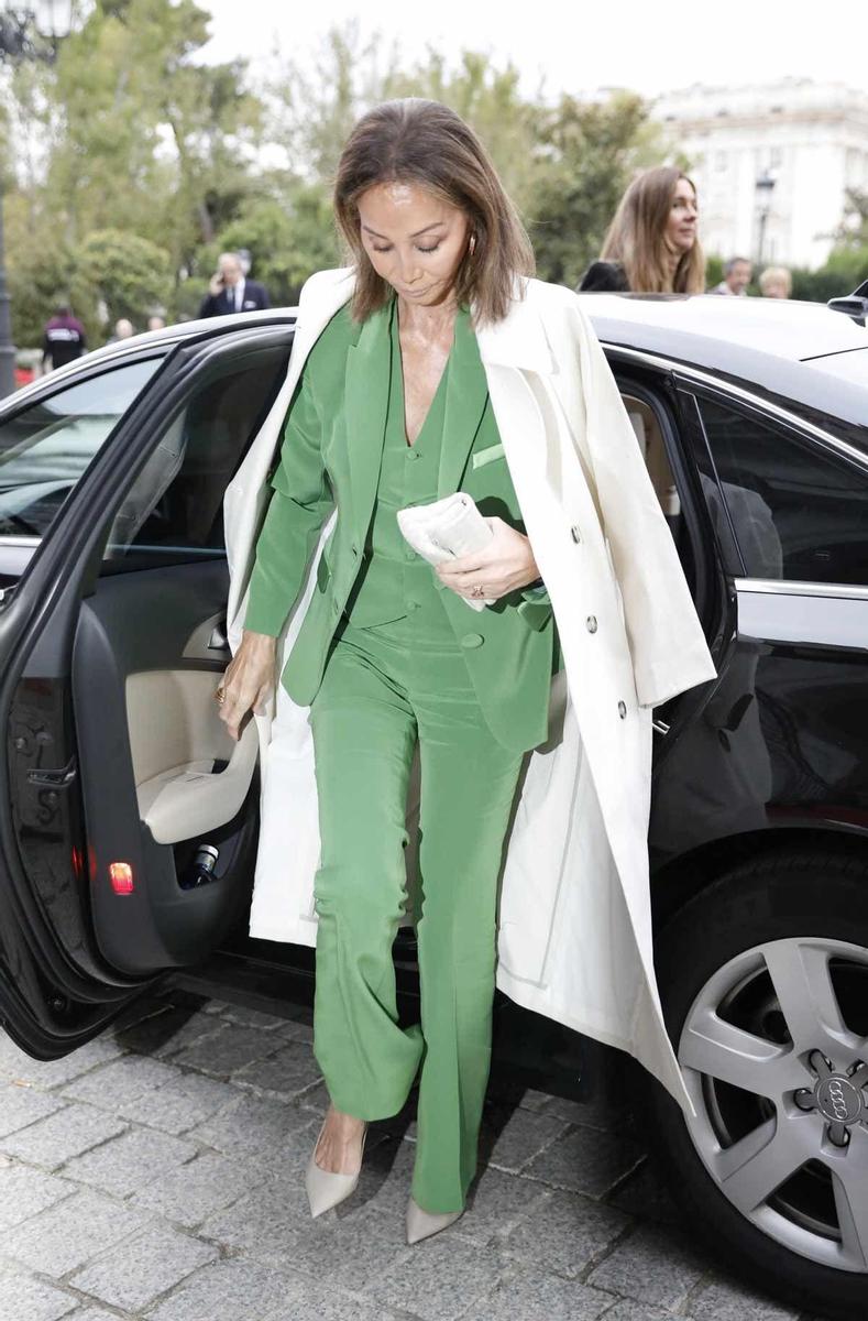 Isabel Preysler con traje pantalón y chaleco verdes y abrigo trench hueso