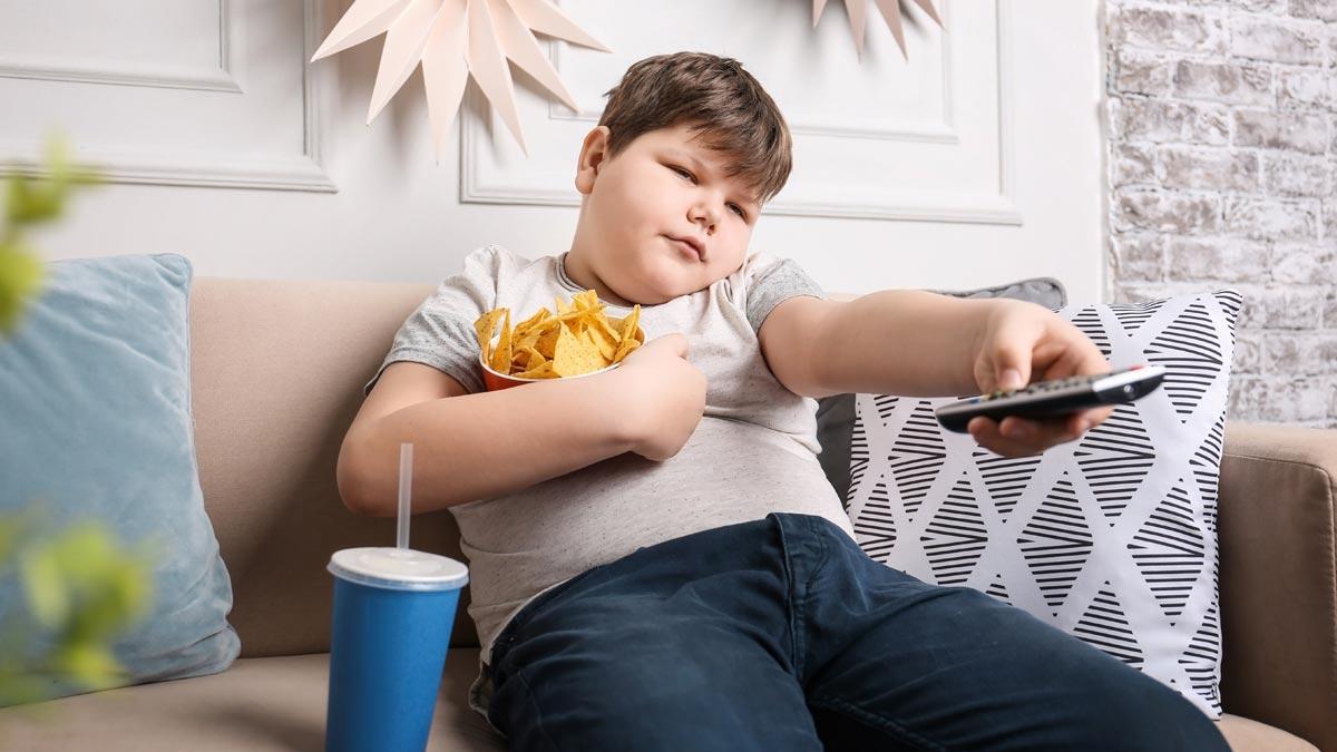 Un niño obeso come mientras ve la televisión
