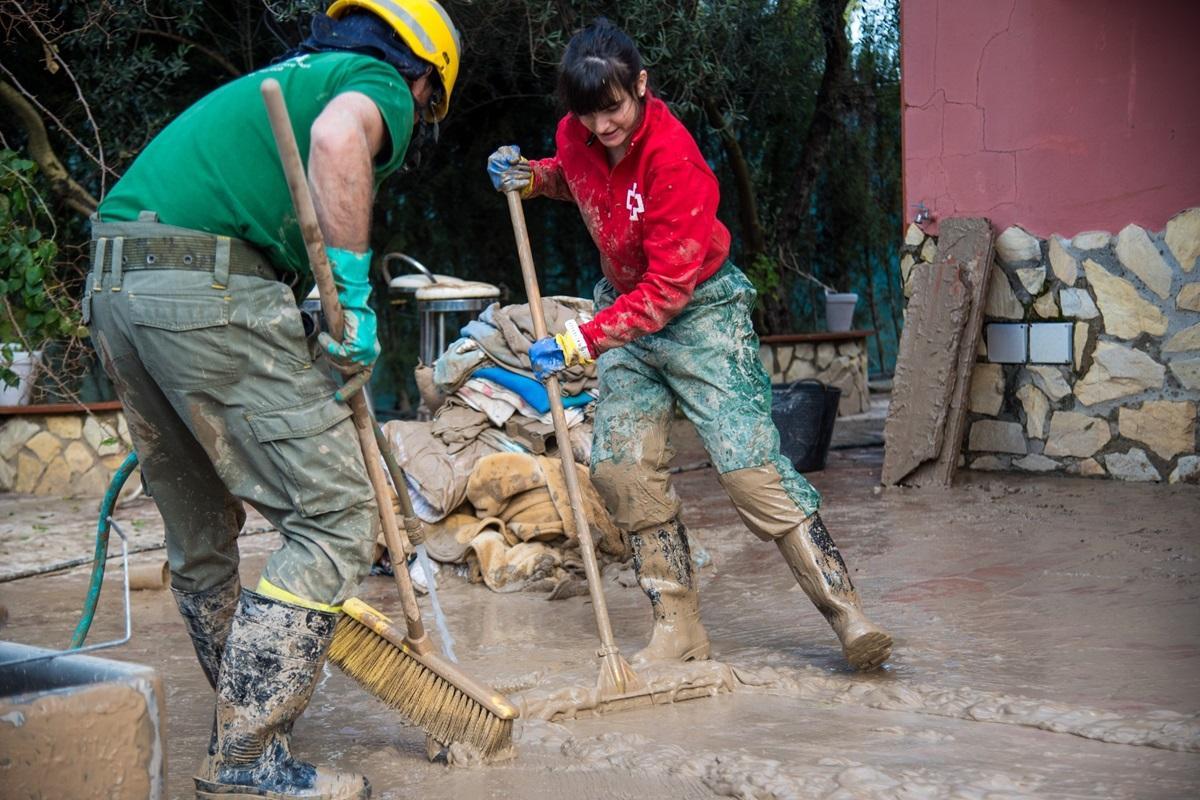 Una voluntaria de Cruz Roja y un trabajador del Infoca limpian de lodo una calle de Palma del Río.