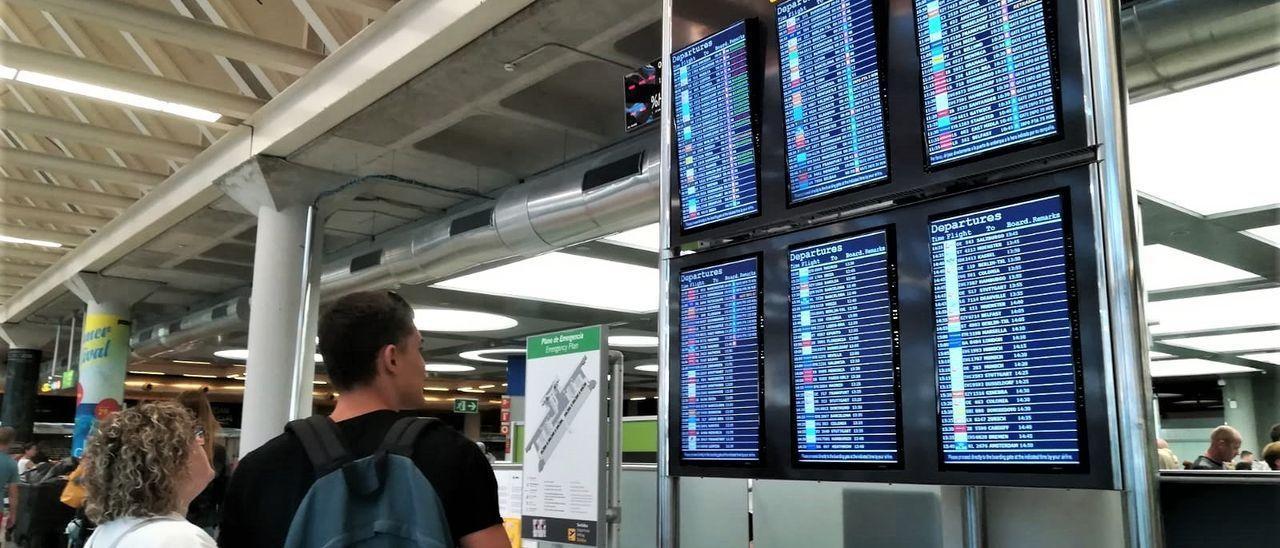 Archivo - Turistas comprueban la información de las pantallas de embarque en el aeropuerto de Palma.