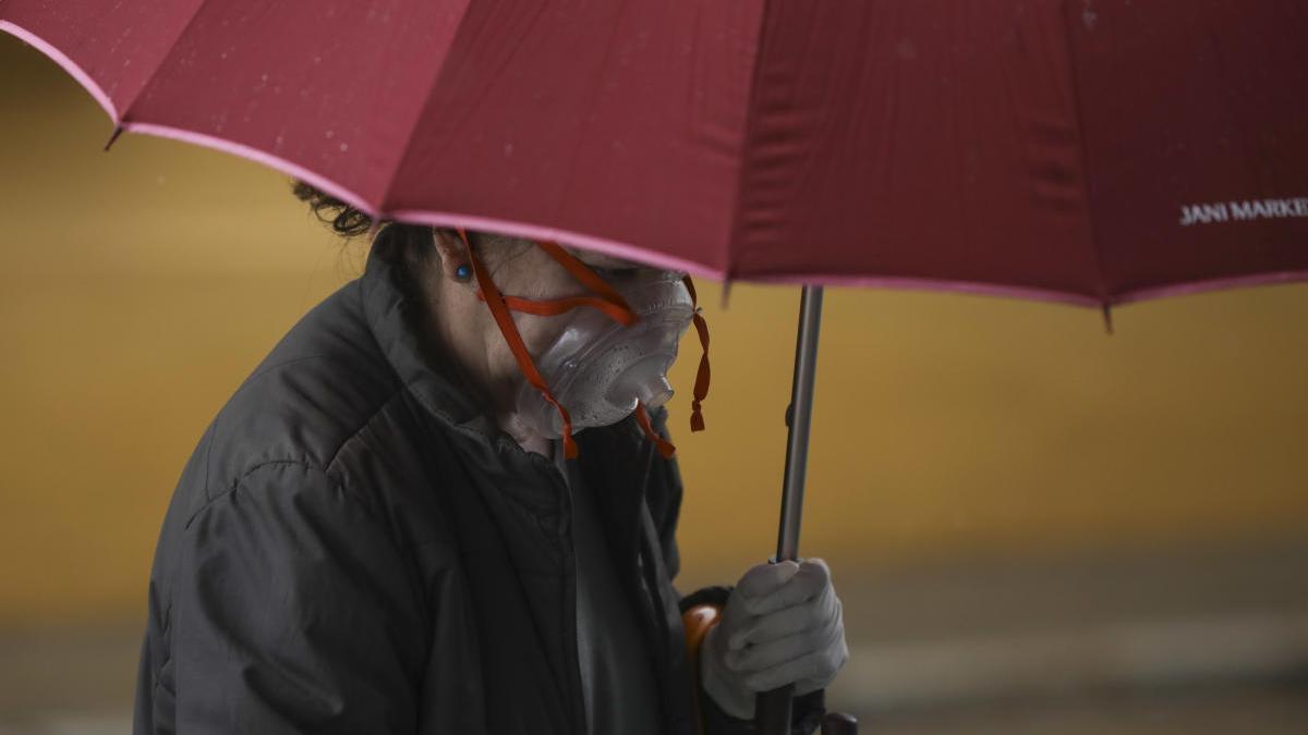 Una mujer camina por la calle protegida con su mascarilla y un paraguas.
