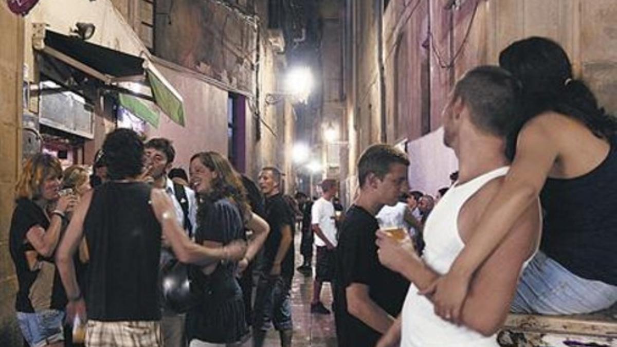 Grupos de jóvenes consumen alcohol y departen en plena calle ante un bar del Raval.