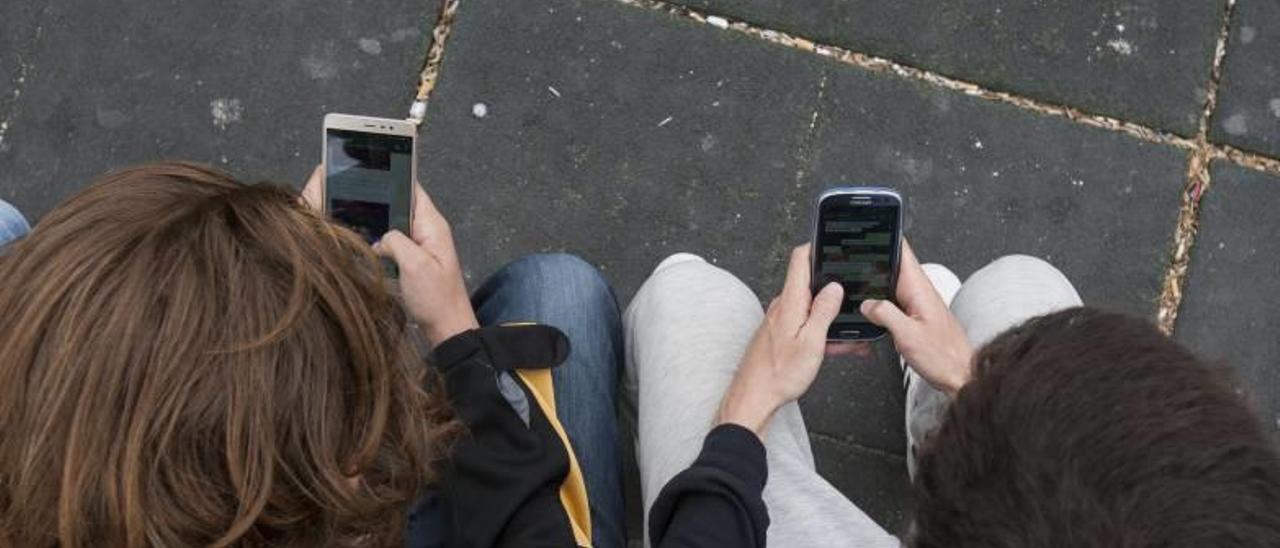 Dos adolescentes usando su terminal móvil en la calle.