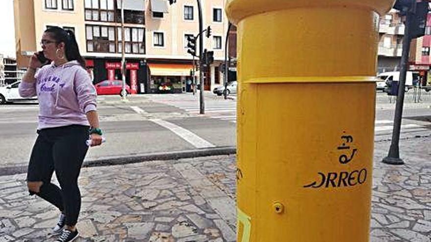 Una joven pasa junto a un buzón de Correos mensajeando con su móvil.