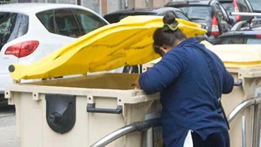 Una mujer busca en el contenedor de la basura.