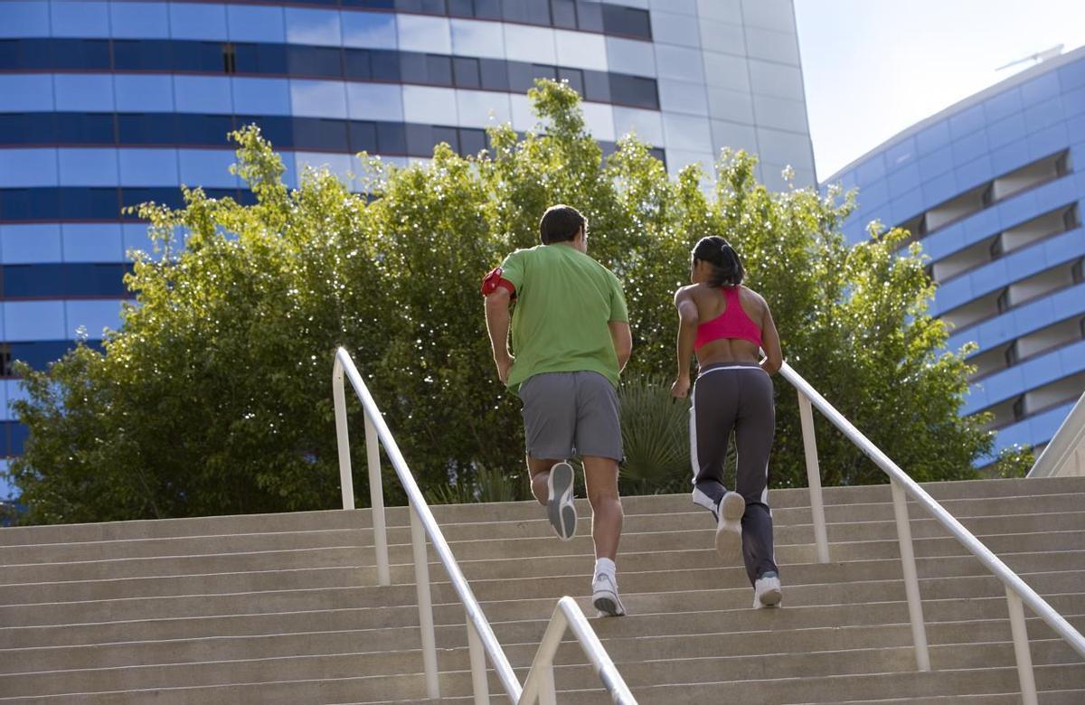 Pareja corriendo escaleras arriba en un entorno urbano, vista trasera