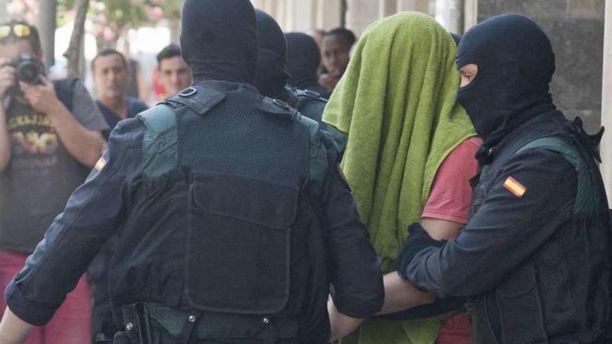 Dos agentes de la Guardia Civil trasladan a uno de los detenidos cubierto con una toalla. // Efe