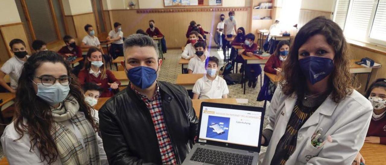 Por la izquierda, Ana Dávila, Joaquín González Cabrera y Marta Tirado muestran en el portátil una diapositiva del programa sobre “ciberbullying”, con los alumnos de 1.º de la ESO del colegio Dulce Nombre de Jesús de Oviedo tras ellos. | Luisma Murias