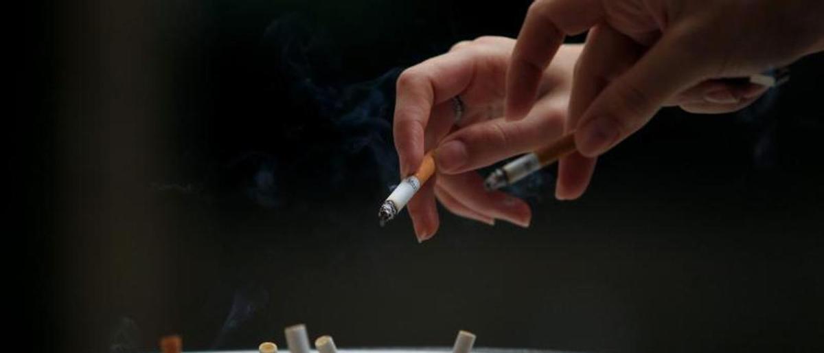 Dos fumadores echan ceniza en un cenicero