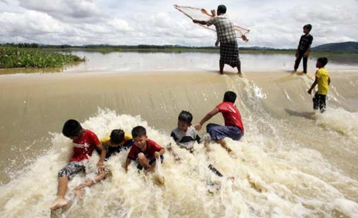 Uns nens juguen a l’aigua mentre un home llança la seva xarxa de pesca en una zona afectada per les inundacions al sud de la província de Pattani (Tailàndia).